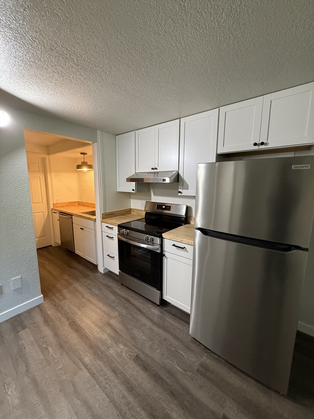 A finished ADU kitchen with white shaker cabinets, butcher block counters and a vented range hood